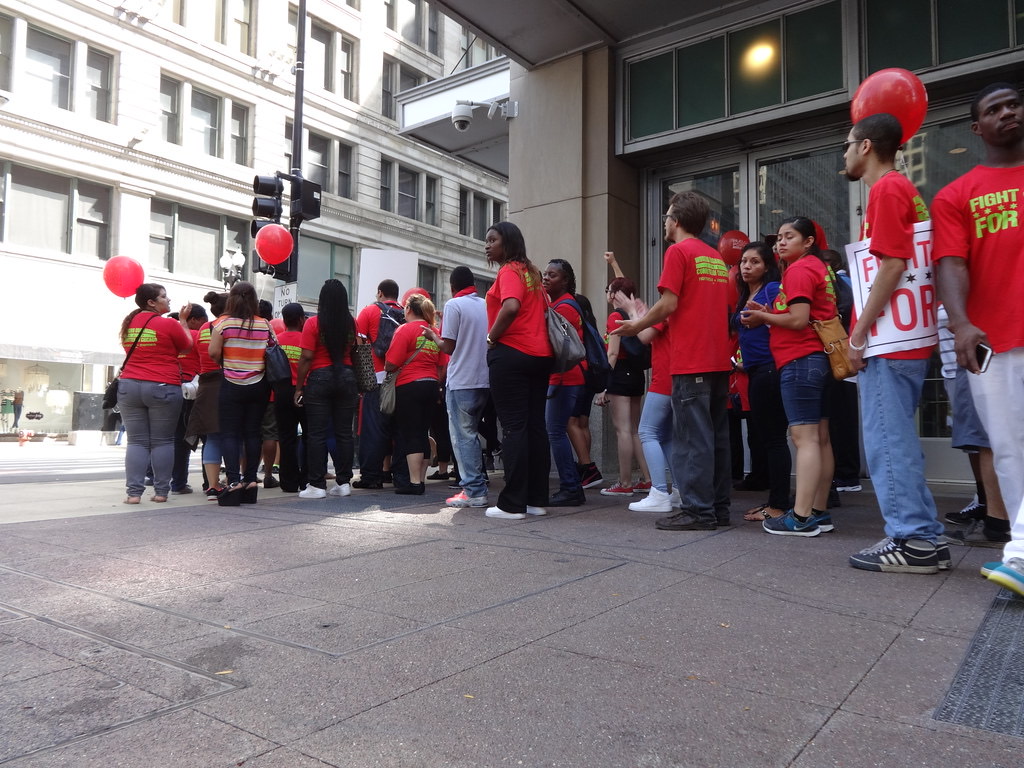 Workers and students rally outside a fast food restaurant holding Fight for 15 placards
